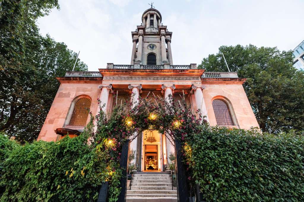 Historic pink building exterior with classical columns, tower, and flowering vines framing the entrance.
