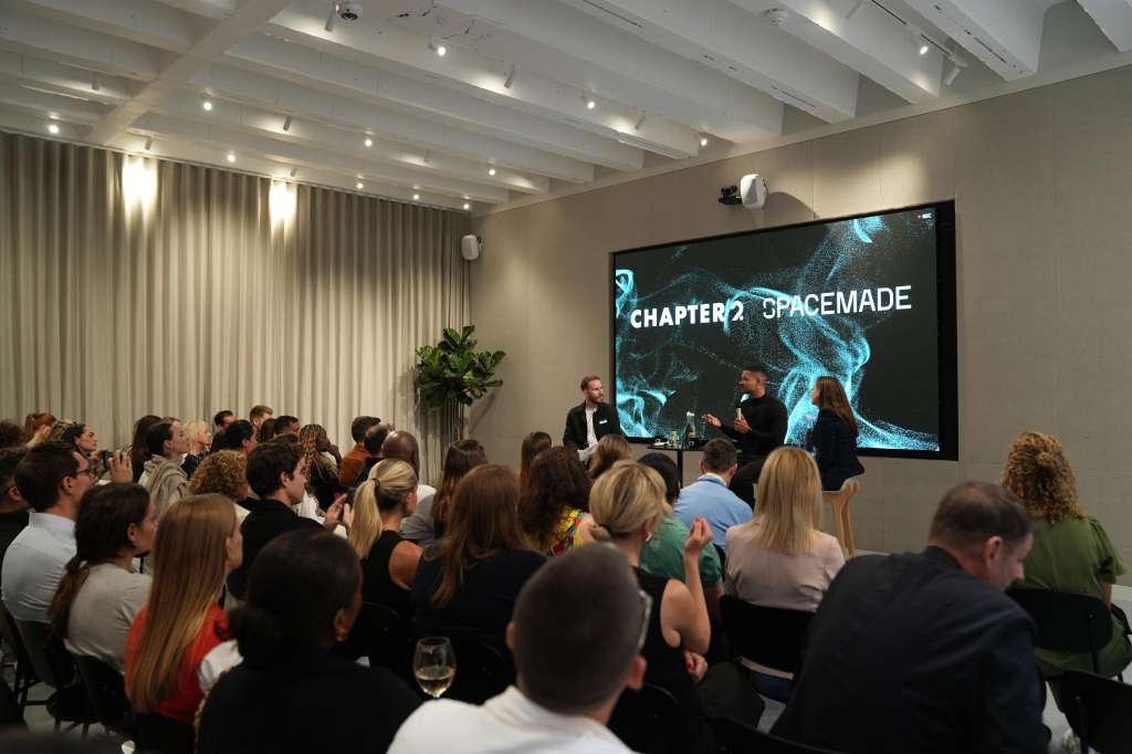 Cormack room with seated audience facing a stage, large projection screen displaying Chapter 2 Spacemade branding, and panelists at front.