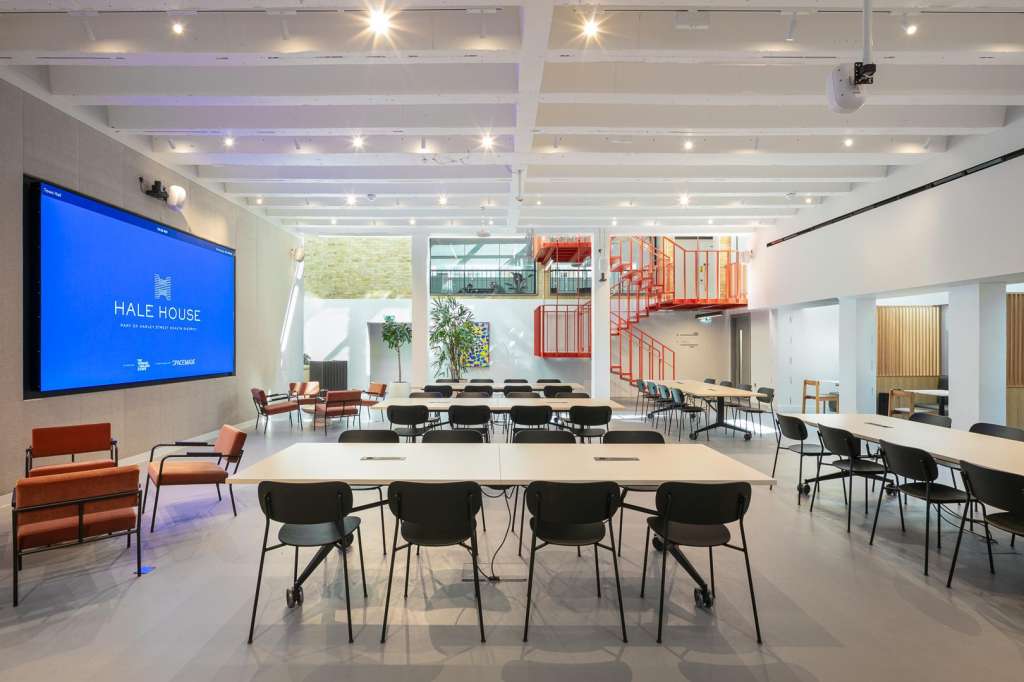 Modern meeting space with rectangular tables, black chairs, large screen displaying Hale House branding, and bright ceiling lights.