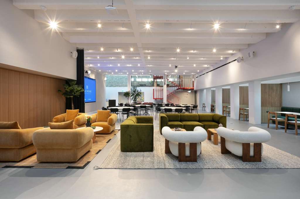 Modern open-plan space with lounge seating, dining area, and meeting tables under coffered ceiling with recessed lighting.