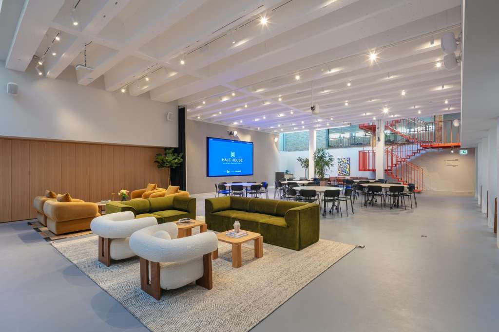 Modern open-plan space with lounge seating, dining tables, and presentation screen under coffered ceiling with accent lighting.