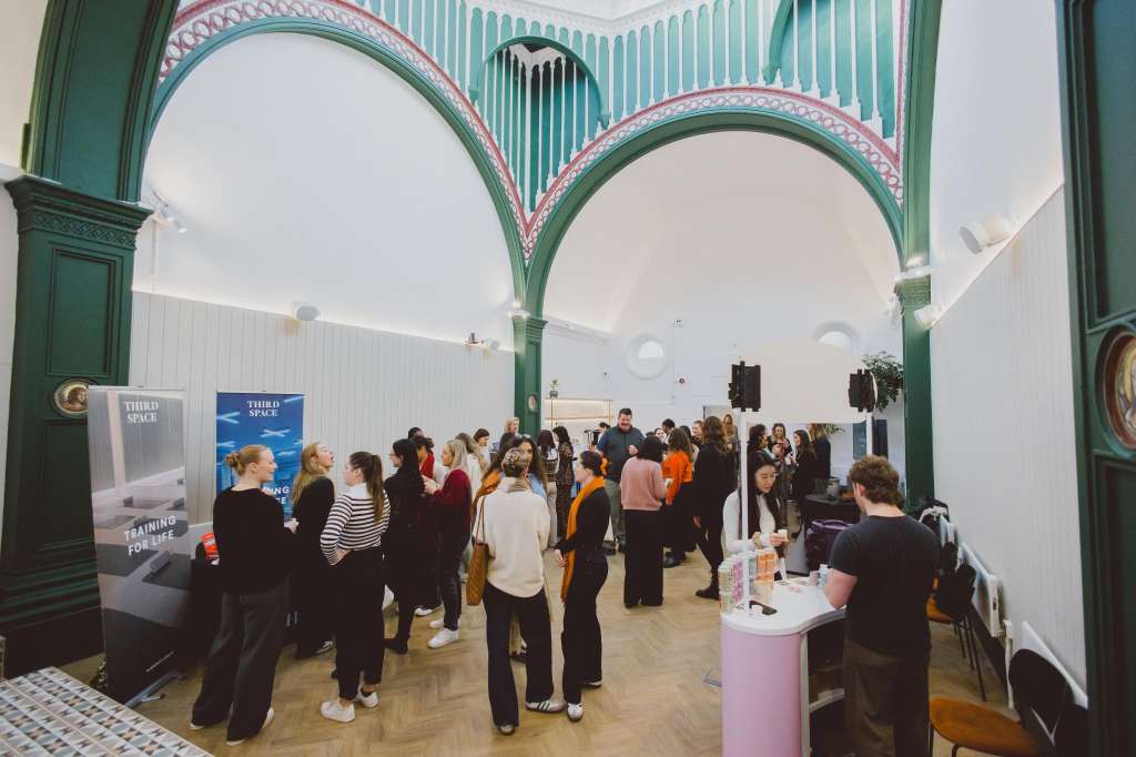 The Chapel interior with green arches and white vaulted ceiling, set up for an exhibition with multiple visitors and display stands.