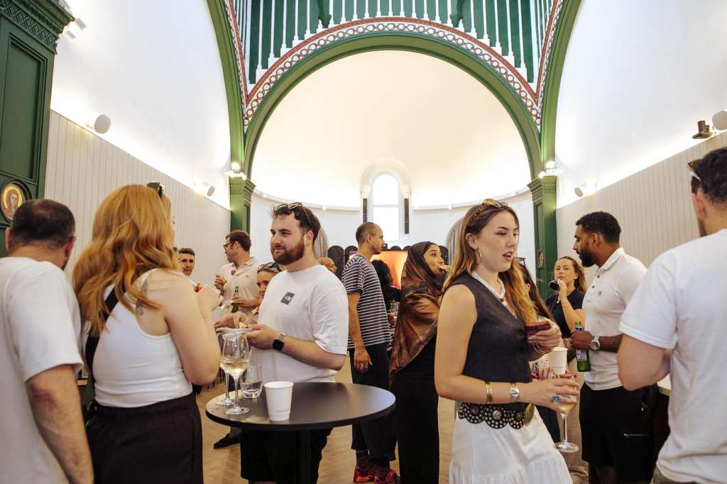 The Chapel interior with guests mingling, holding drinks at high tables under a green arched ceiling with decorative details.