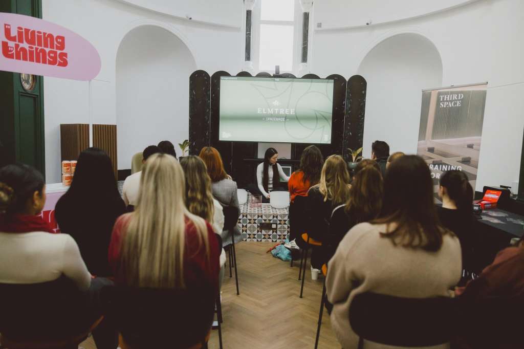 Chapel interior with seated audience facing a screen displaying Elmtree branding, arched windows and green door visible.