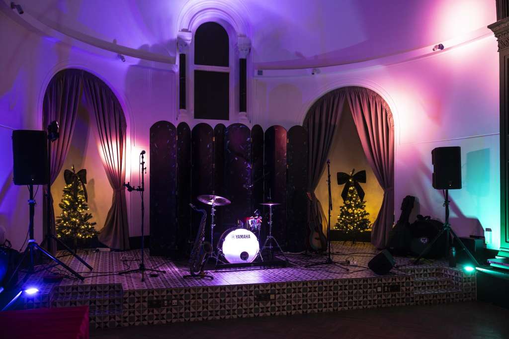 The Chapel set up for an event with stage, drum kit, speakers, and dynamic purple and pink lighting.