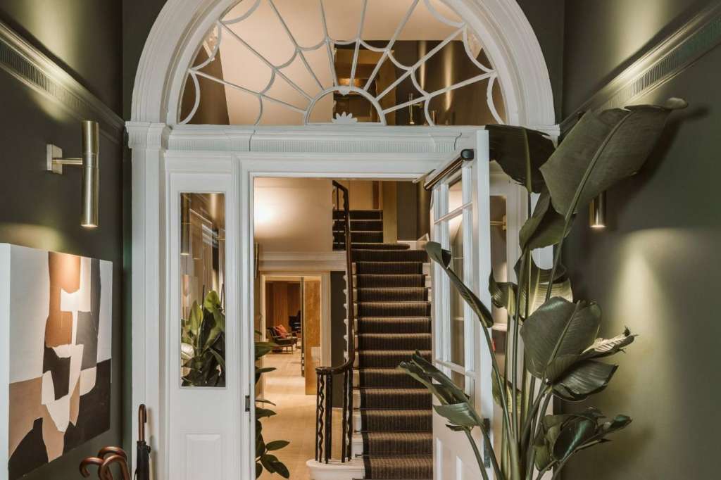 Elegant entrance hallway with arched fanlight door, green walls, potted plants, and staircase visible beyond.