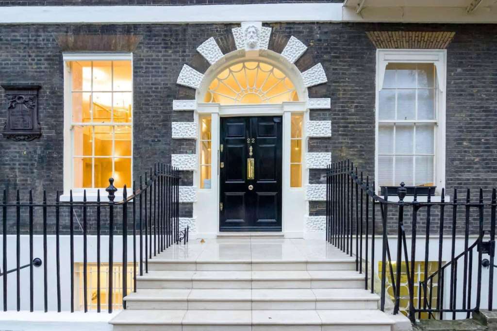 Exterior facade of Georgian townhouse with black door, fanlight, brick walls, and iron railings.