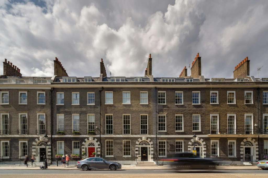 Georgian townhouse facade with brick exterior, sash windows, and ornamental stonework on a London street.