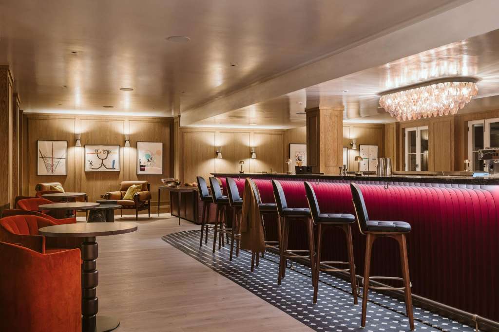 Bar and lounge area with red upholstered seating, wooden paneling, crystal chandelier, and modern lighting throughout.