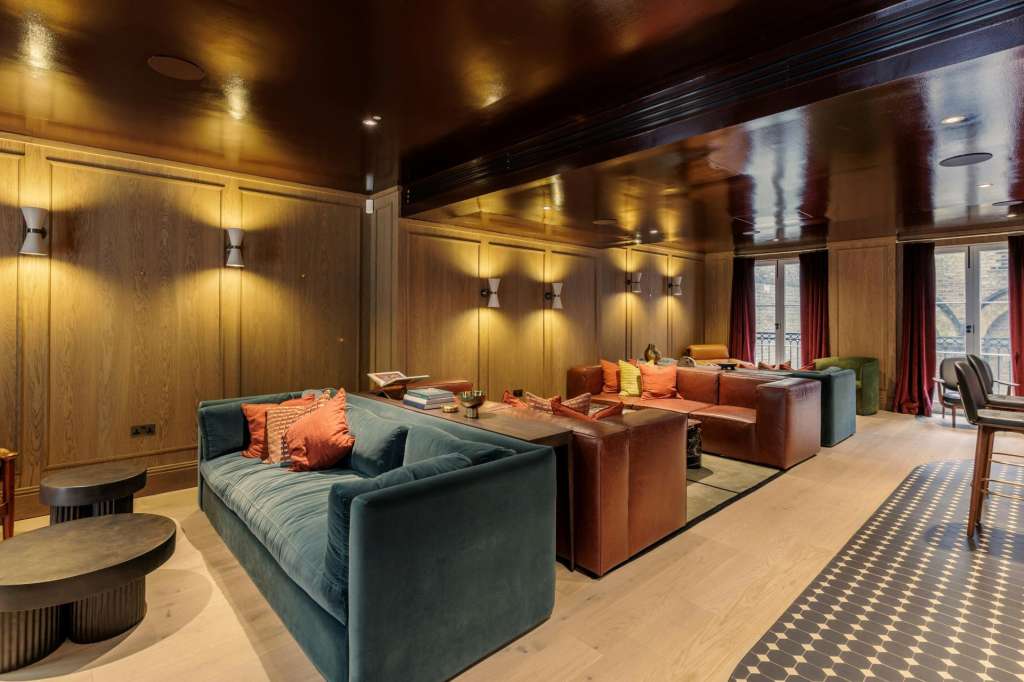 The Bar with lounge seating, warm wood paneling, ambient lighting, and large windows with red curtains.
