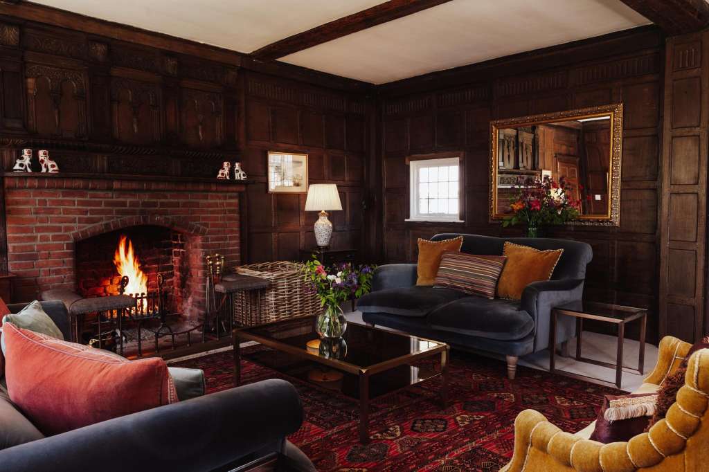 Wood-paneled lounge with fireplace, dark sofas, gold cushions, ornate mirror, and warm lighting.