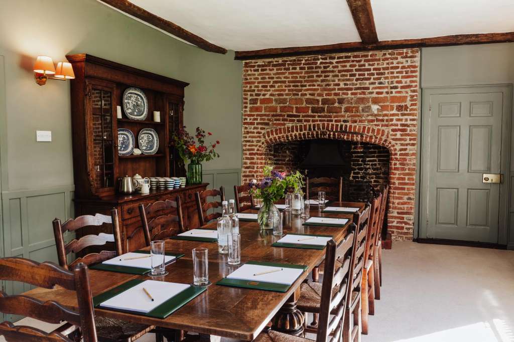 The Grainstore set up for a seated meeting or meal with long wooden table, place settings, water glasses, and fireplace backdrop.
