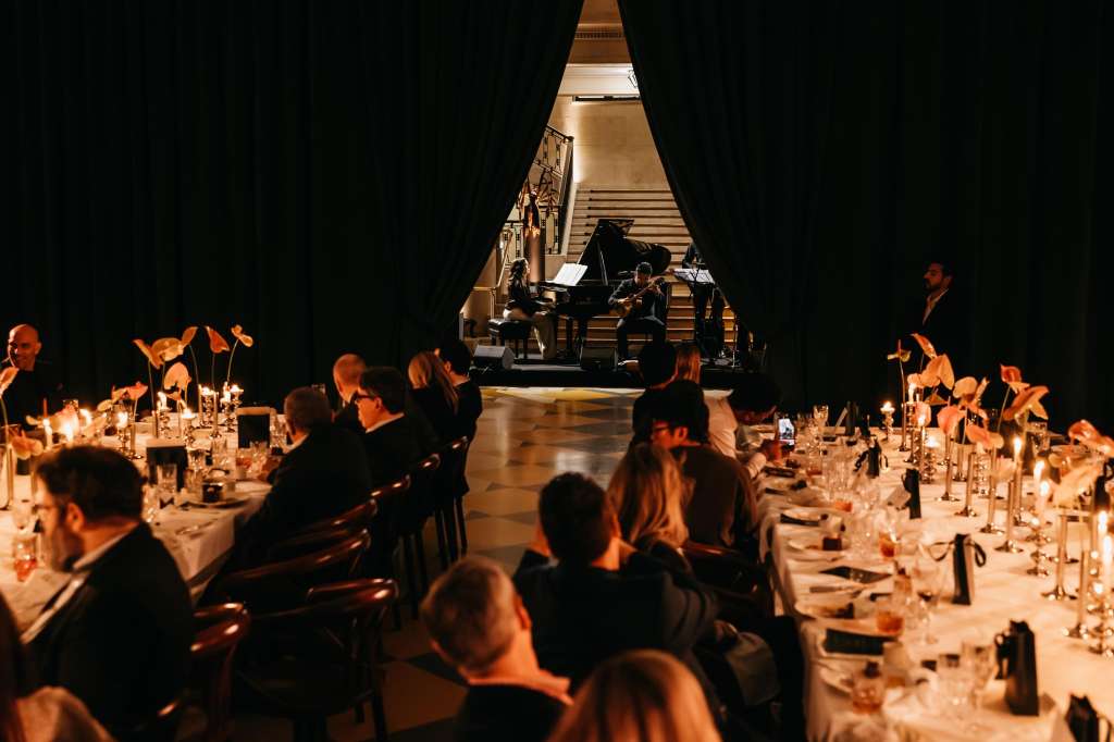 Main Hall set for formal dinner with long tables, candlelight, and live piano performance on stage.