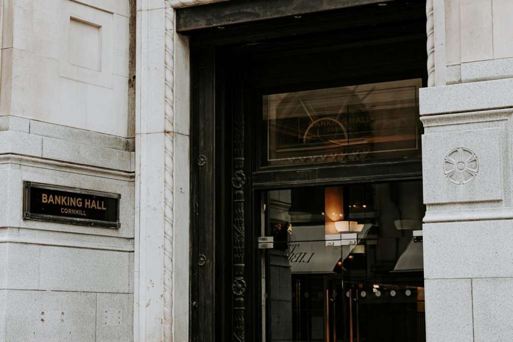 Exterior entrance to Banking Hall with stone facade, black ornate door, and brass plaque signage.