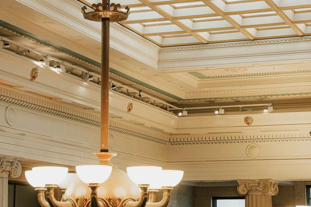 The Main Hall with ornate coffered ceiling, brass chandelier, fluted columns, and classical architectural details.