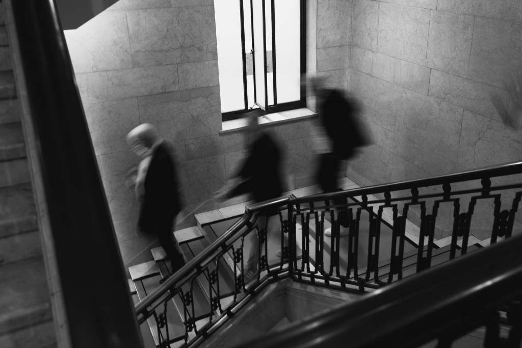 Blurred figures descending a staircase with metal railings in a stone-walled corridor.