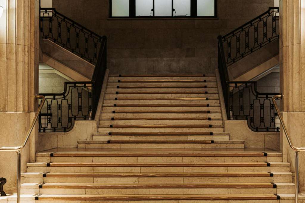 Grand staircase in marble hall with symmetrical railings, decorative floor medallion, and art deco geometric patterns.