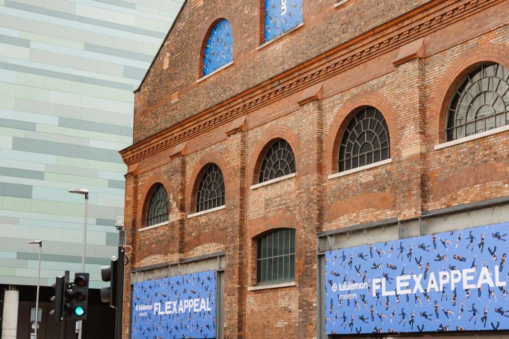 Exterior of historic red-brick building with blue signage and crowd gathered at entrance.