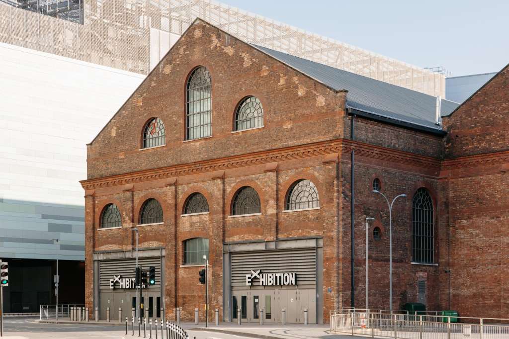 Exterior of historic red brick building with arched windows and metal roller doors labeled Exhibition.
