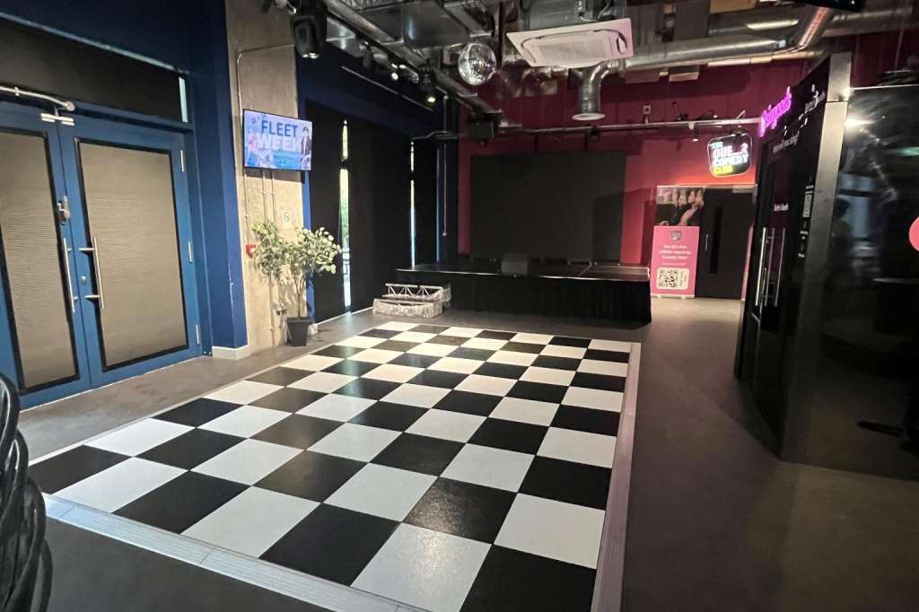 Main space with black and white checkered dance floor, stage, professional lighting rig, and neon signage.