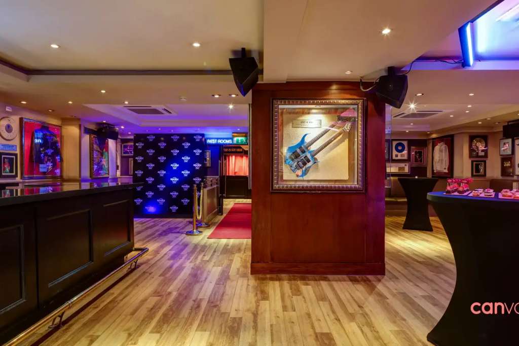 The Rock Room interior with bar counter, framed music memorabilia on walls, blue ambient lighting, and high-top cocktail tables.