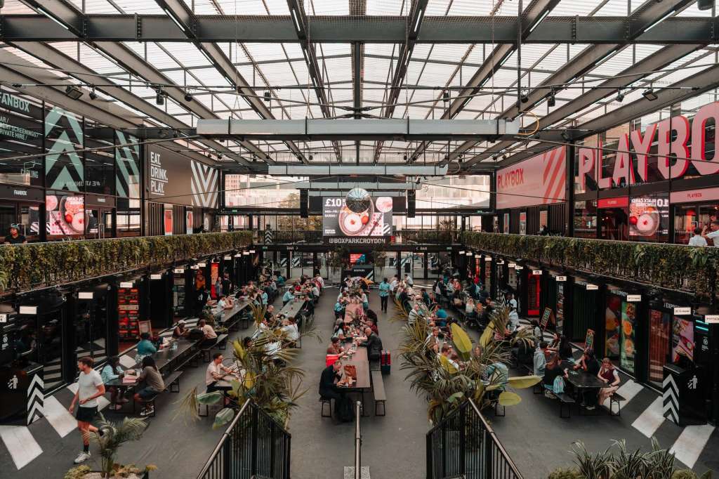 Indoor market hall with glass roof, food stalls, seating areas, and crowds of visitors browsing and dining.