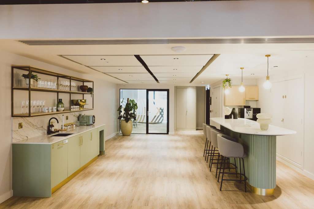 Modern hospitality space with curved bar counter, open kitchen, shelving, pendant lighting, and natural wood flooring.