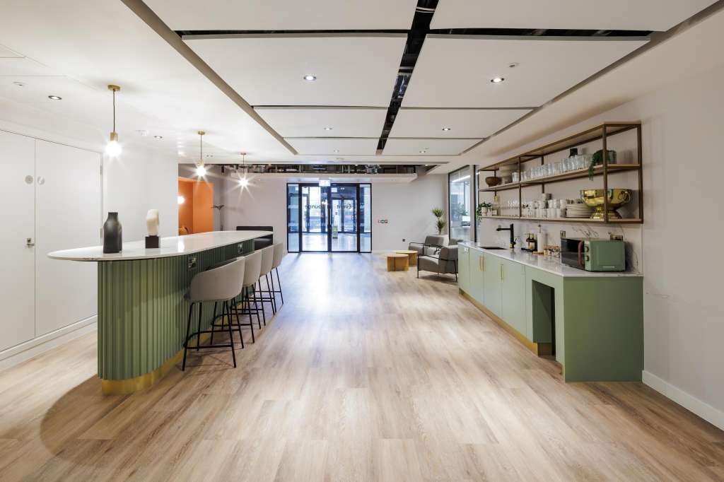 Modern open-plan space with green bar counter, shelving, pendant lighting, and wood flooring. Styled for hospitality or events.