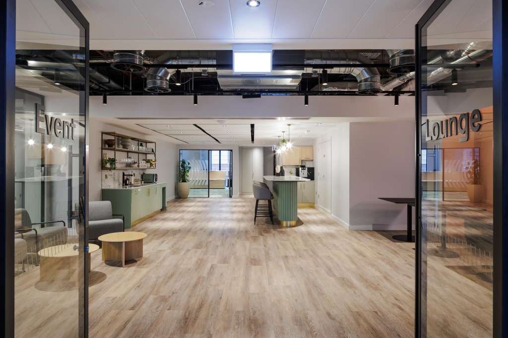 Modern open-plan event space with wood flooring, glass partitions, lounge seating, and contemporary lighting.