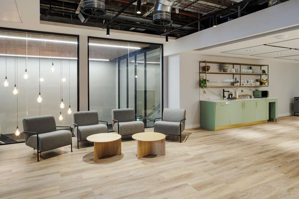 Modern lounge space with gray armchairs, wooden side tables, pendant lighting, and green bar counter.
