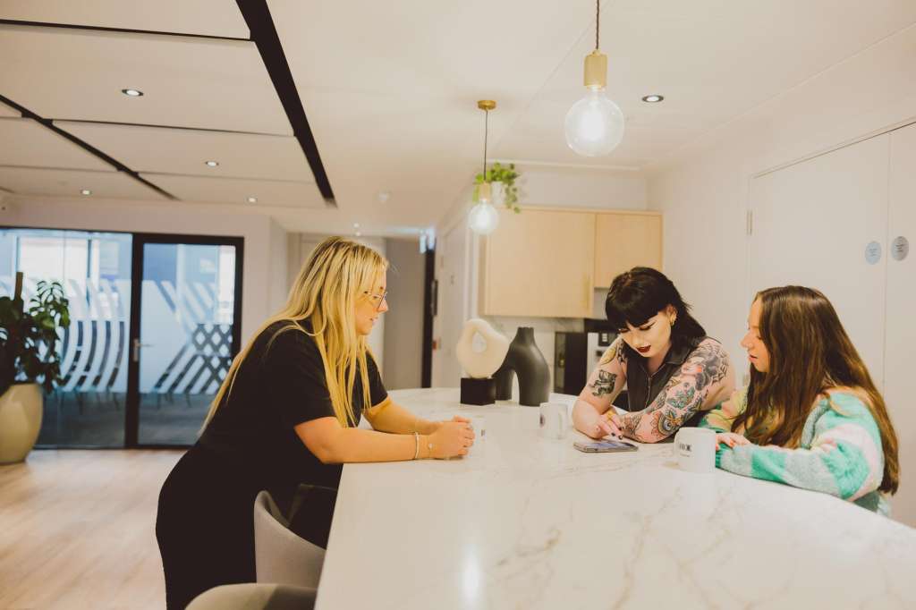 Modern office space with three people seated at a white marble counter, pendant lighting, and floor-to-ceiling windows.