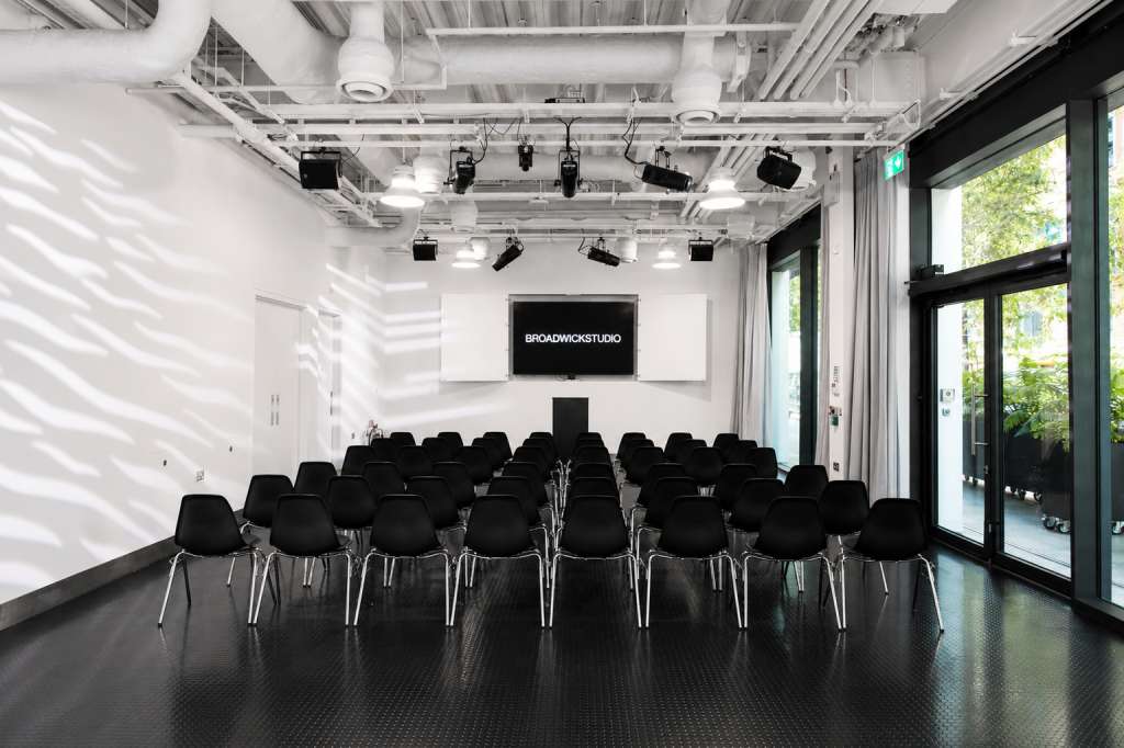 Main space with rows of black chairs facing a screen displaying Broadwick Studio logo, industrial ceiling with spotlights.