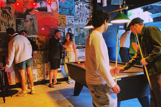 Interactive exhibition space with colorful posters, gaming stations, and visitors engaging with displays under dramatic lighting.