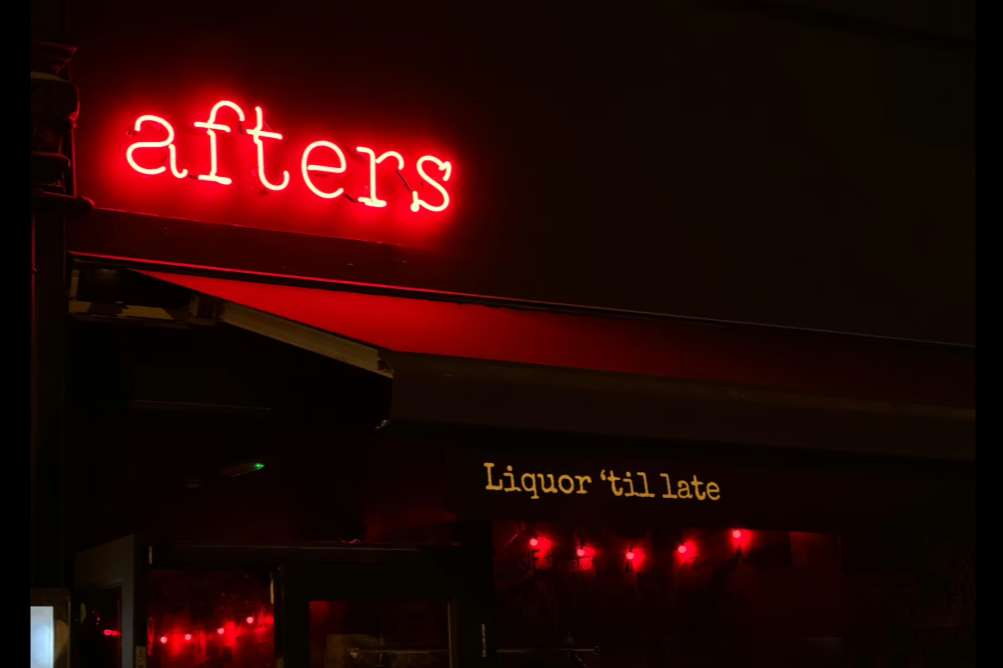 Exterior storefront with red neon 'afters' sign and decorative red lights at night.