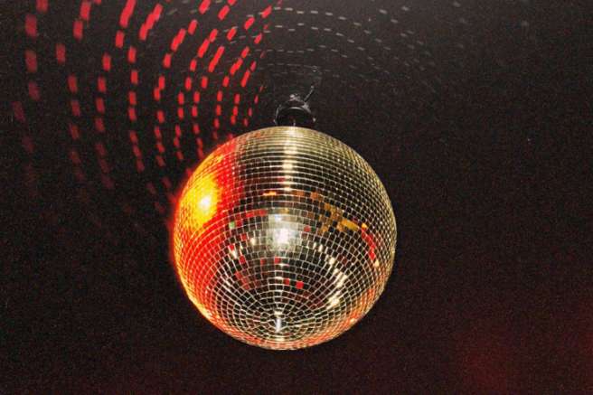 Illuminated disco ball with red light projections on dark ceiling and colorful signage below.