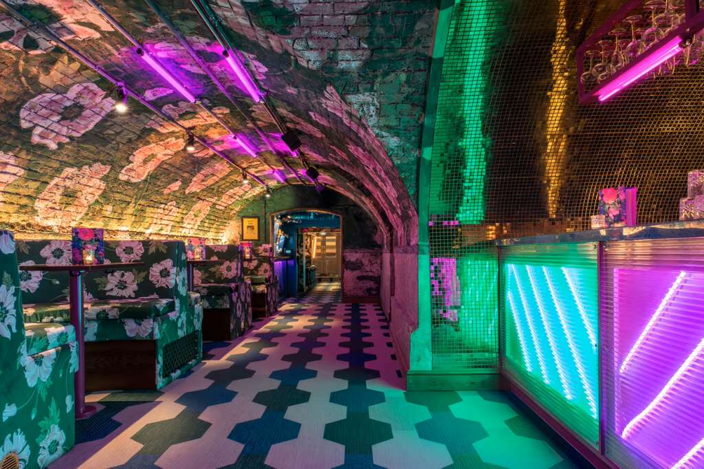 Back Bar with neon lighting, geometric floor, floral booth seating, and vibrant pink and green ambient lighting.