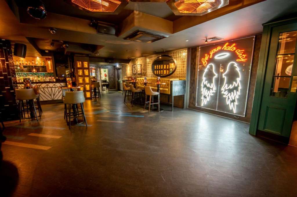 Upscale bar and lounge with neon signage, high-top seating, brick walls, and warm ambient lighting throughout.