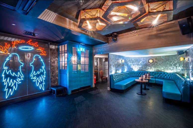 VIP lounge with blue neon signage, tufted seating, geometric ceiling lights, and moody blue ambient lighting.