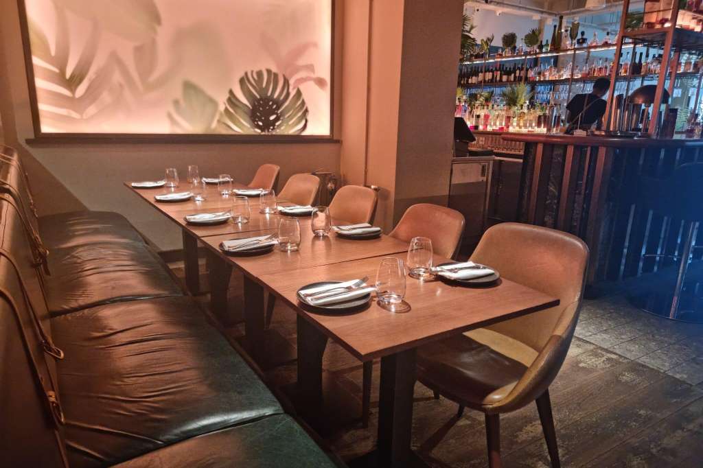Private dining room with long wooden table, place settings, leather banquette seating, and botanical wall art.
