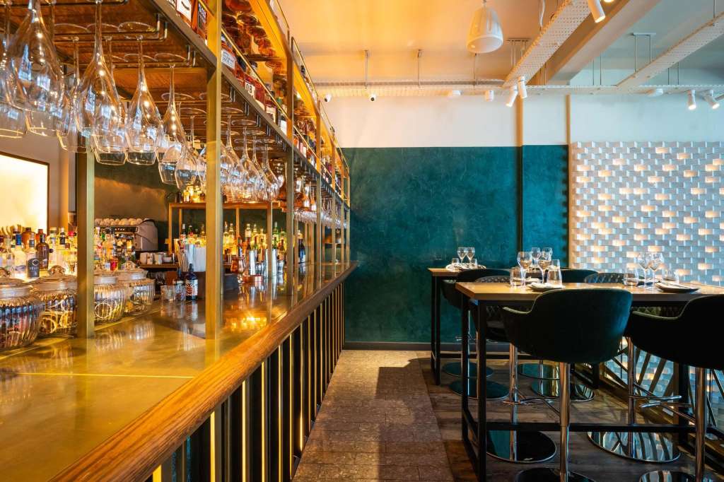 Private dining room with bar counter, high-top seating, teal accent wall, and pendant lighting.