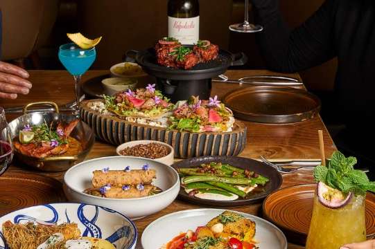 Private dining table set with multiple plated dishes, cocktails, wine, and fresh garnishes.