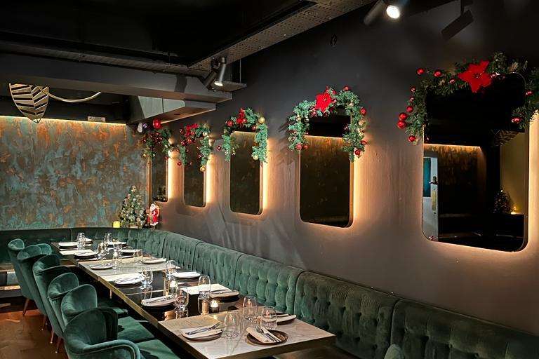 Private dining room with long table, green velvet seating, place settings, and festive red floral garland decorations on illuminated wall panels.
