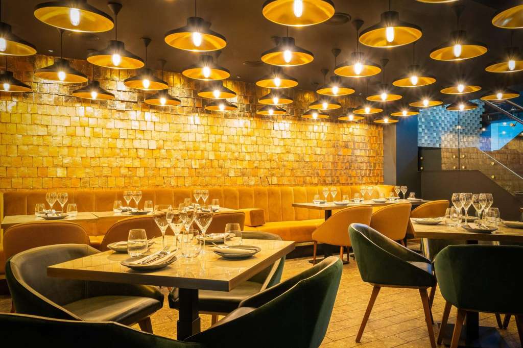 Private dining room with gold pendant lighting, yellow brick walls, place settings, and modern seating arranged for service.