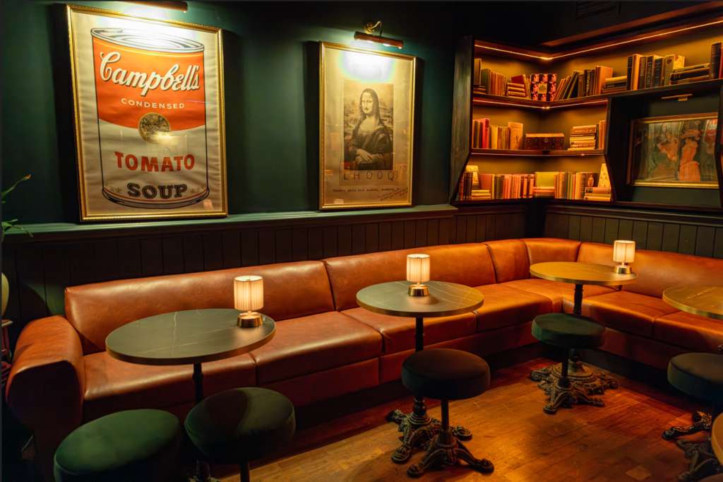 Lounge area with curved cognac leather banquette, small tables, warm ambient lighting, and pop art wall decor.