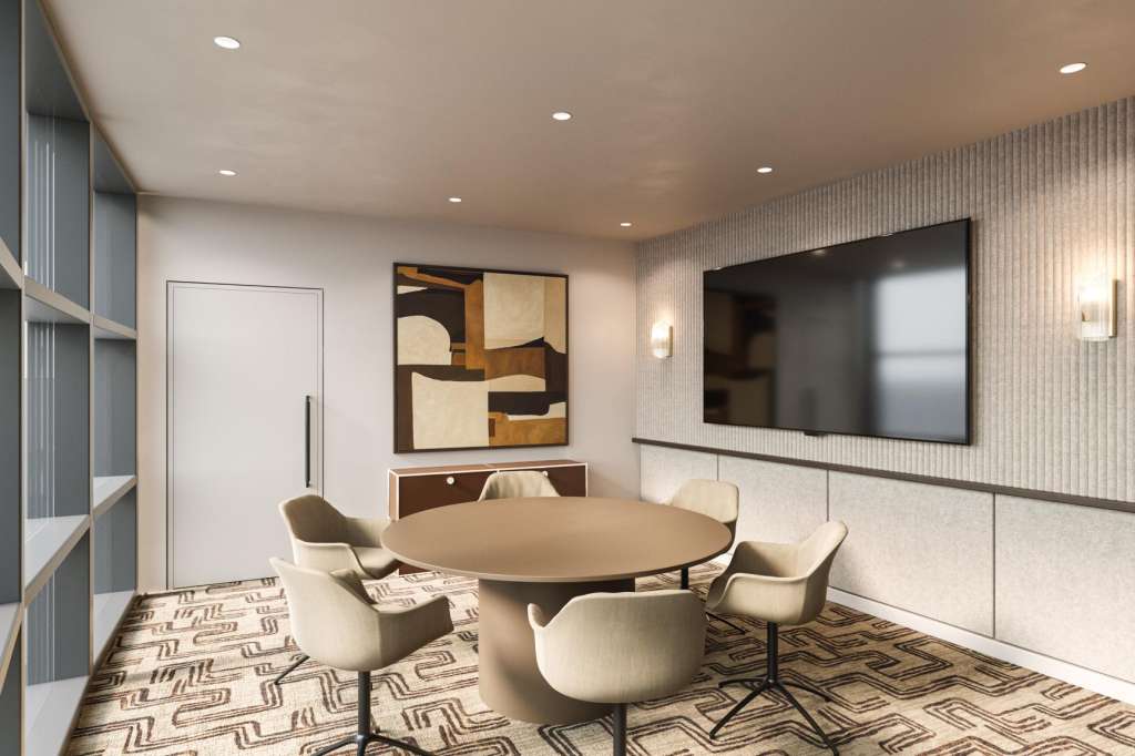 Modern meeting room with round table, four upholstered chairs, large wall-mounted screen, and geometric patterned flooring.