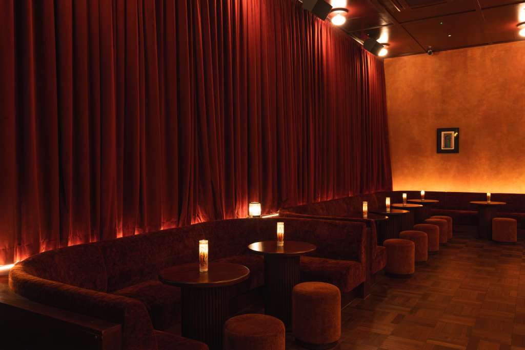 Lounge area with red velvet curtains, warm ambient lighting, round tables, and upholstered seating.