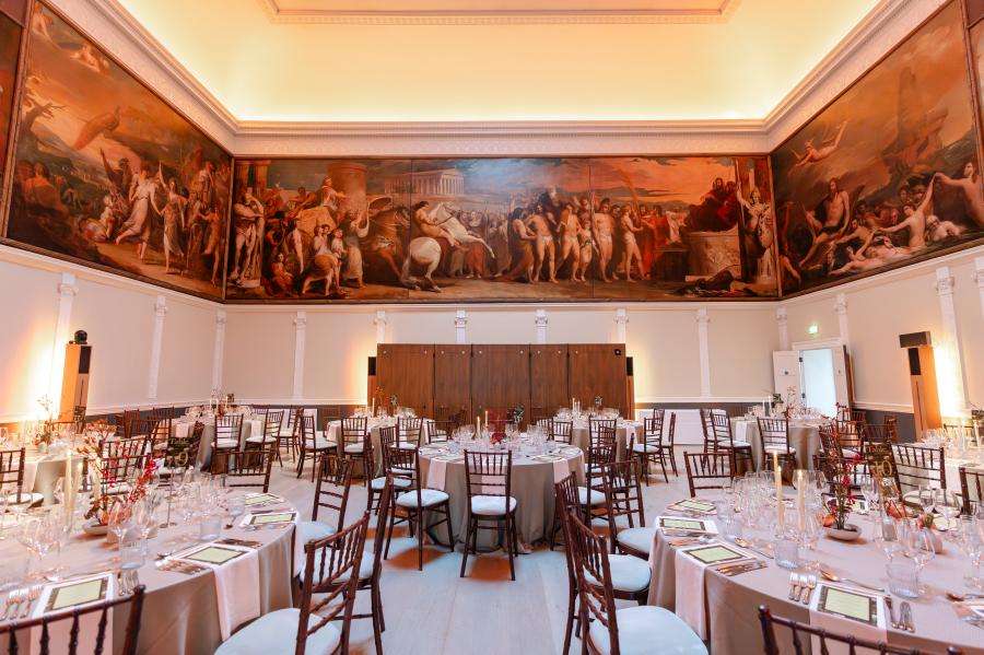 Great Room set for a formal dinner with round tables, chiavari chairs, place settings, and classical murals overhead.