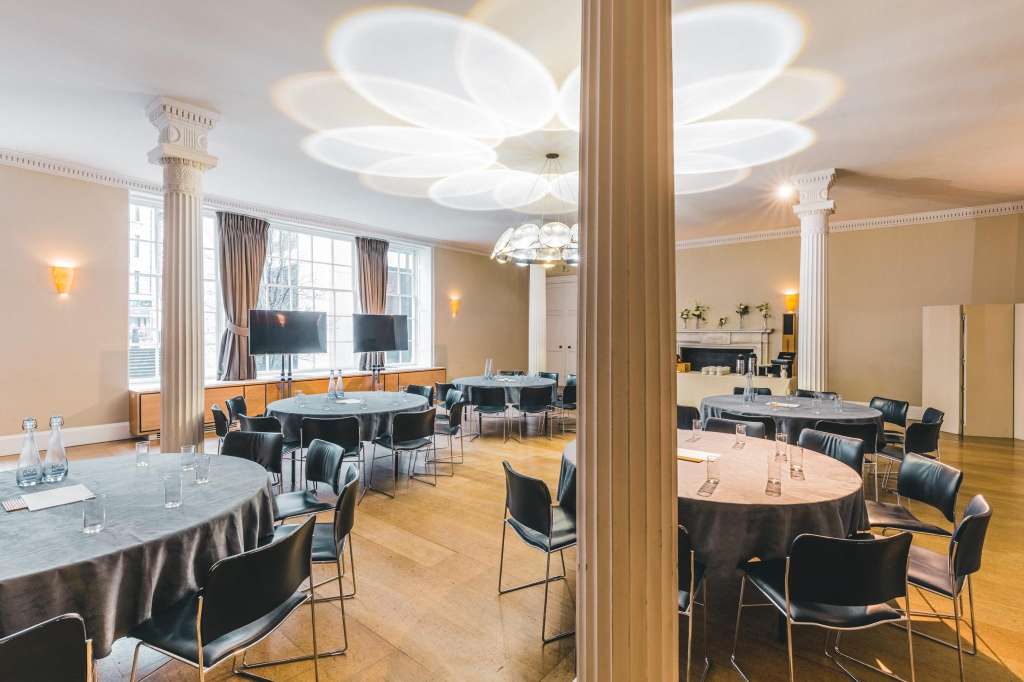 Great Room set up with round tables, black chairs, modern ceiling lights, tall columns, and large windows with curtains.