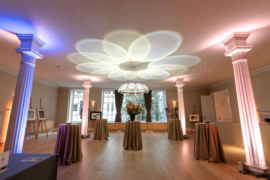 Grand room with tall columns, draped cocktail tables, modern ceiling fixture, and ambient colored lighting.