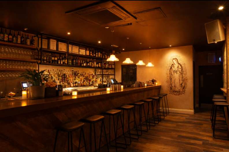 Bar interior with extensive bottle display, warm lighting, bar seating, and decorative wall art.